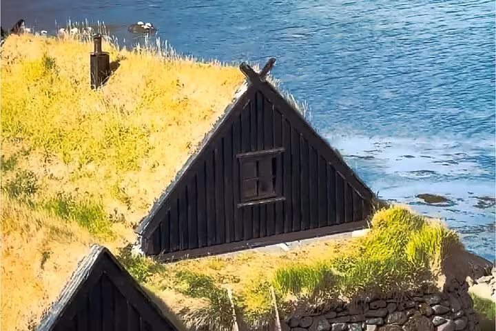Traditional black turf-roofed house on a grassy hillside overlooking the sea in the Westfjords, Iceland