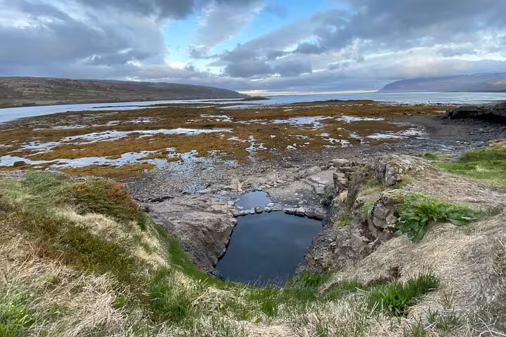 Rocky volcanic pool overlooking Westfjords coastline and fjord under dramatic cloudy sky
