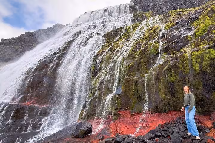 Traveler standing beside a massive cascading waterfall with red rocks in the Westfjords of Iceland