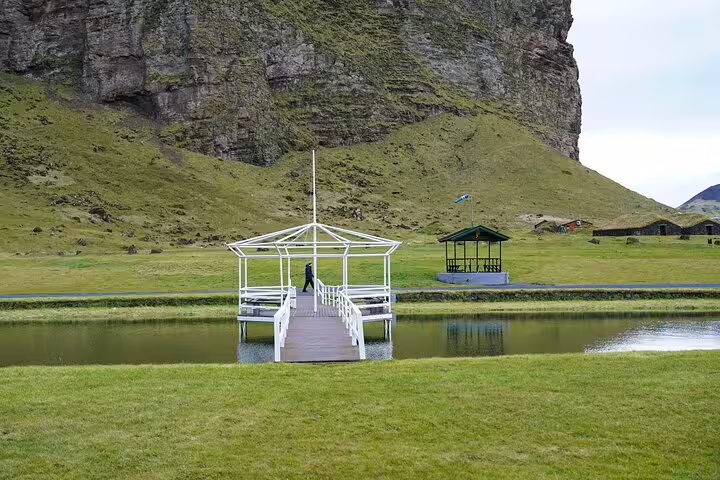 Peaceful pond with white gazebo and dramatic cliffs backdrop on Westman Islands private day tour Iceland