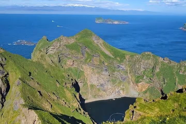 Aerial view of rugged green cliffs and small bay at Westman Islands, Iceland, with ocean and islands in background