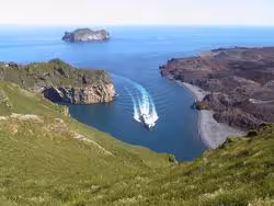Boat cruising through Westman Islands bay with dramatic cliffs and volcanic black sand beach, Iceland