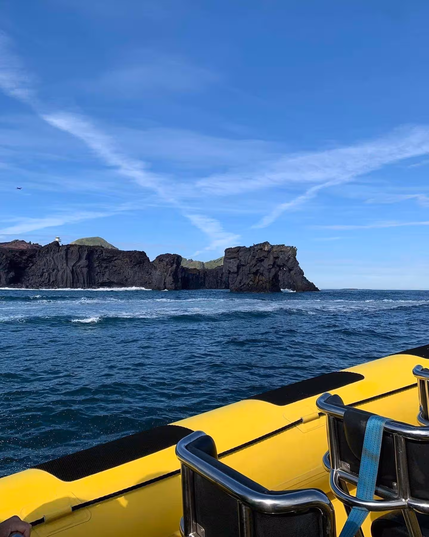 Yellow RIB speedboat approaching dramatic black volcanic cliffs of Westman Islands on a sunny day