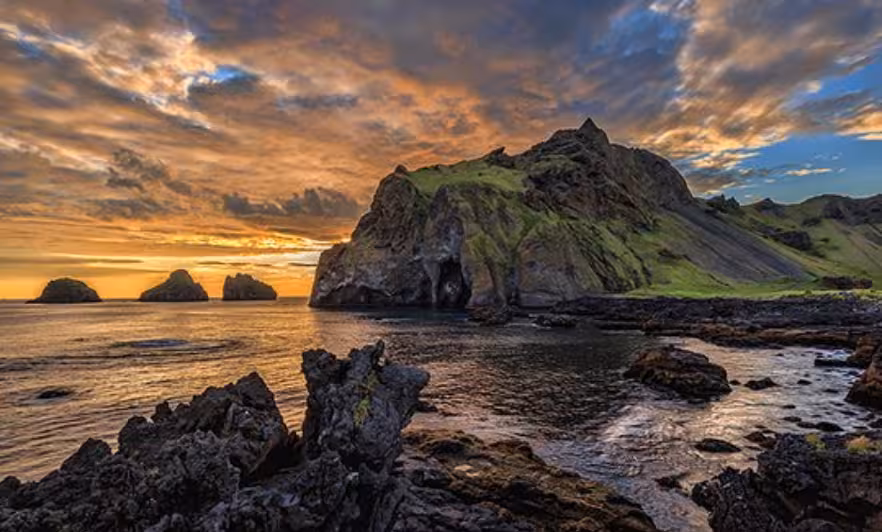 Dramatic sunset over Westman Islands rocky coastline with green cliffs and sea caves