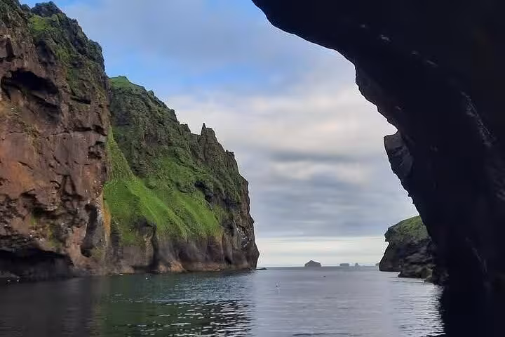 Rocky sea cave opening revealing green moss-covered cliffs and calm ocean waters at Westman Islands Iceland