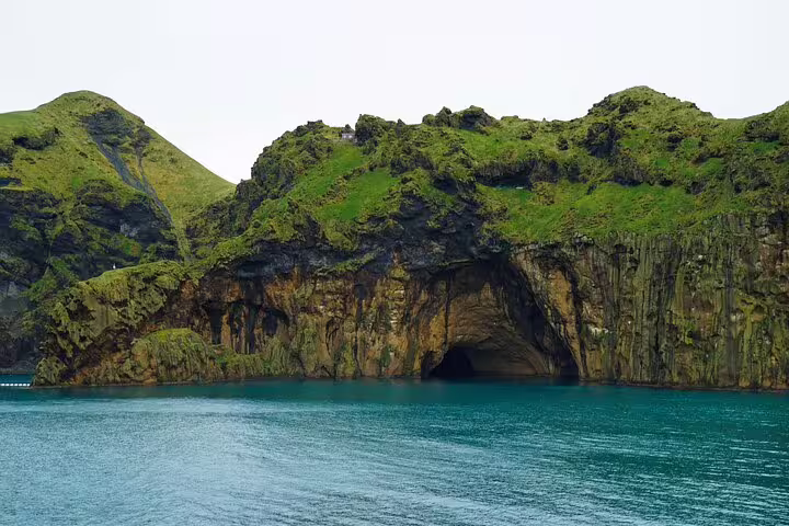 Dramatic Westman Islands sea cave with lush green cliffs and turquoise waters on Iceland volcanic day tour