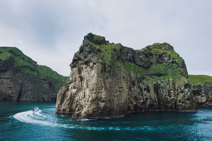 Rocky sea cliffs of Westman Islands with turquoise waters and a small boat passing by, Iceland