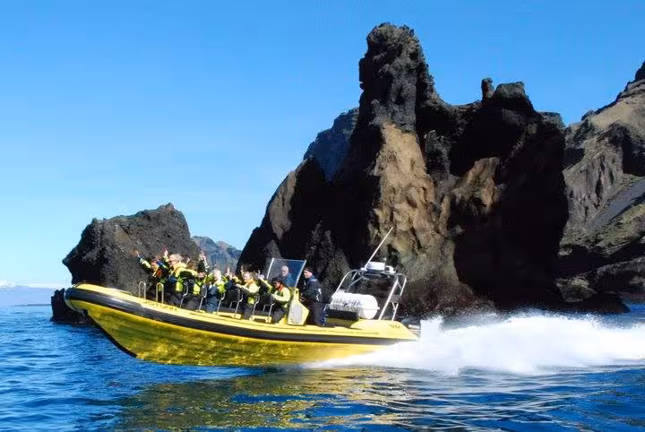 Yellow speedboat with tourists navigating rocky Westman Islands sea cliffs on a sunny day