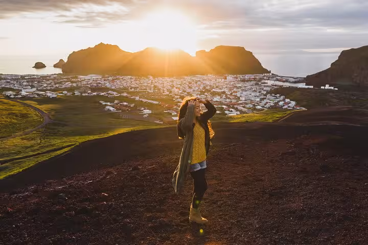 Woman standing on volcanic hillside overlooking Westman Islands town at golden sunset