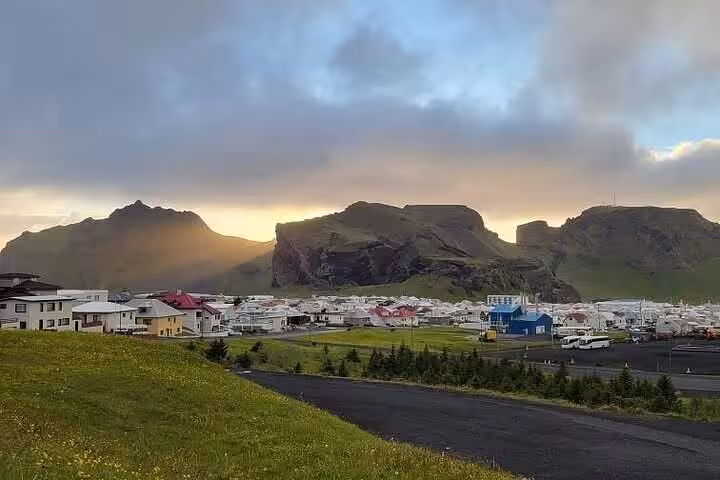 Panoramic view of Westman Islands town with colorful buildings nestled below dramatic volcanic mountains at sunset