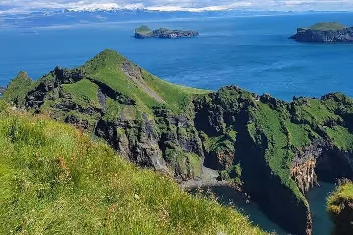 Green volcanic cliffs and rocky coastline of Westman Islands with small islands and blue ocean in background