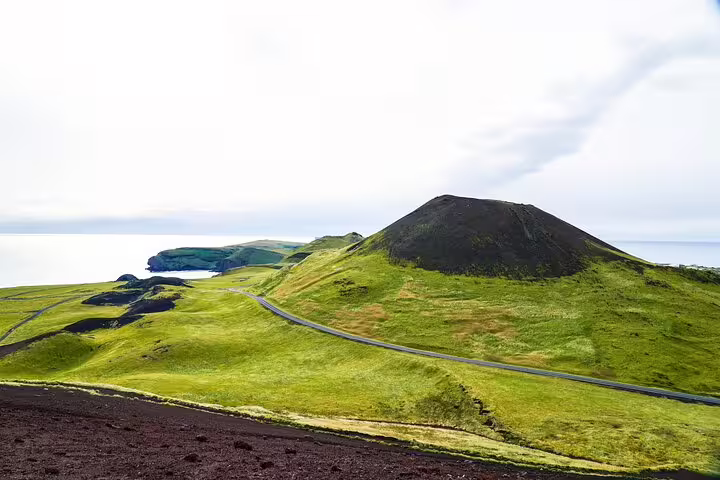 Scenic volcanic crater and winding road through lush green hills on Westman Islands volcanic wonders day tour