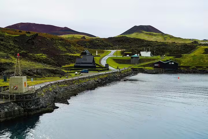 Scenic Westman Islands harbor with volcanic hills, black church, and calm blue waters on a private day tour