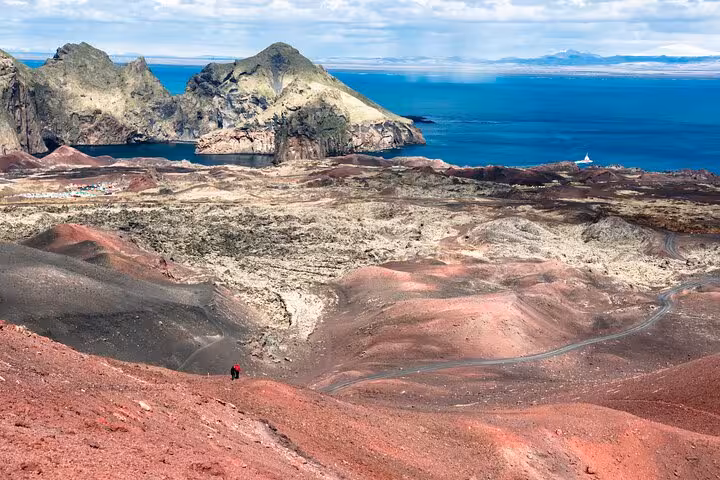 Aerial view of volcanic red lava fields and rocky coastline of Westman Islands, Iceland with two hikers