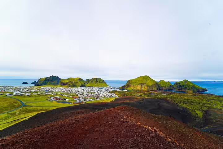 Aerial view of Westman Islands volcanic landscape with red lava fields green hills and coastal town of Heimaey Iceland
