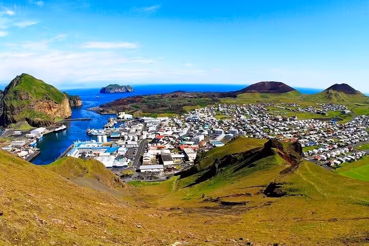 Aerial panoramic view of Westman Islands town with colorful houses, harbor, volcanic hills, and blue ocean