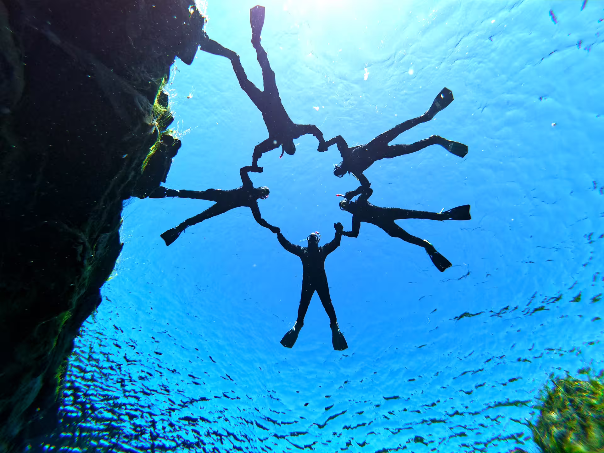 Snorkelers form a circle in crystal-clear Silfra waters, showcasing unique underwater adventure from Reykjavik with wetsuits and photos.