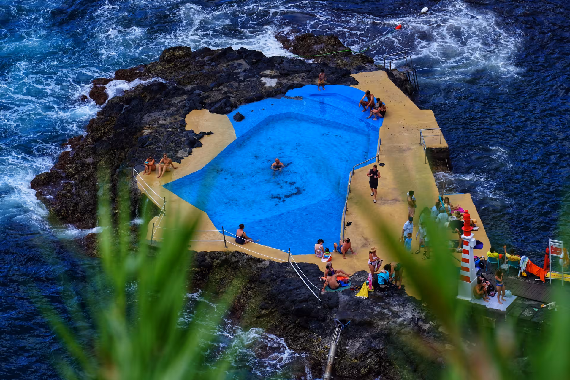 Travelers relaxing by a natural ocean pool and rocky coastline in Caloura after whale watching and water activities
