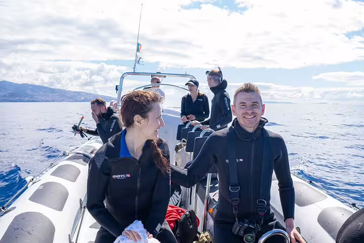 Tourists enjoy a whale and dolphin watching adventure on a boat off the coast of Funchal, Madeira, under a clear sky.