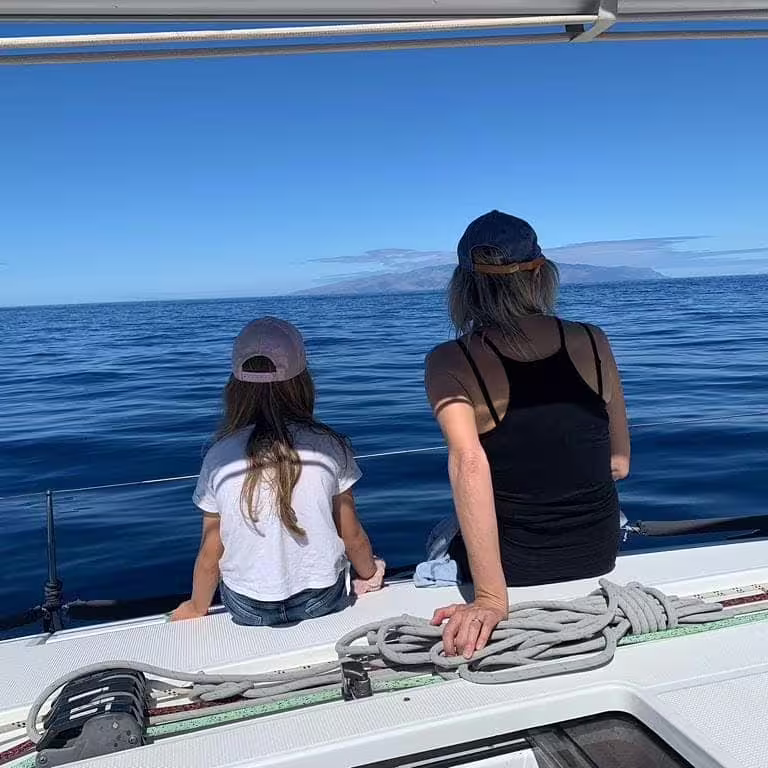 Two people sitting on a yacht deck enjoying a serene whale and dolphin watching trip in Puerto Colón under clear skies.