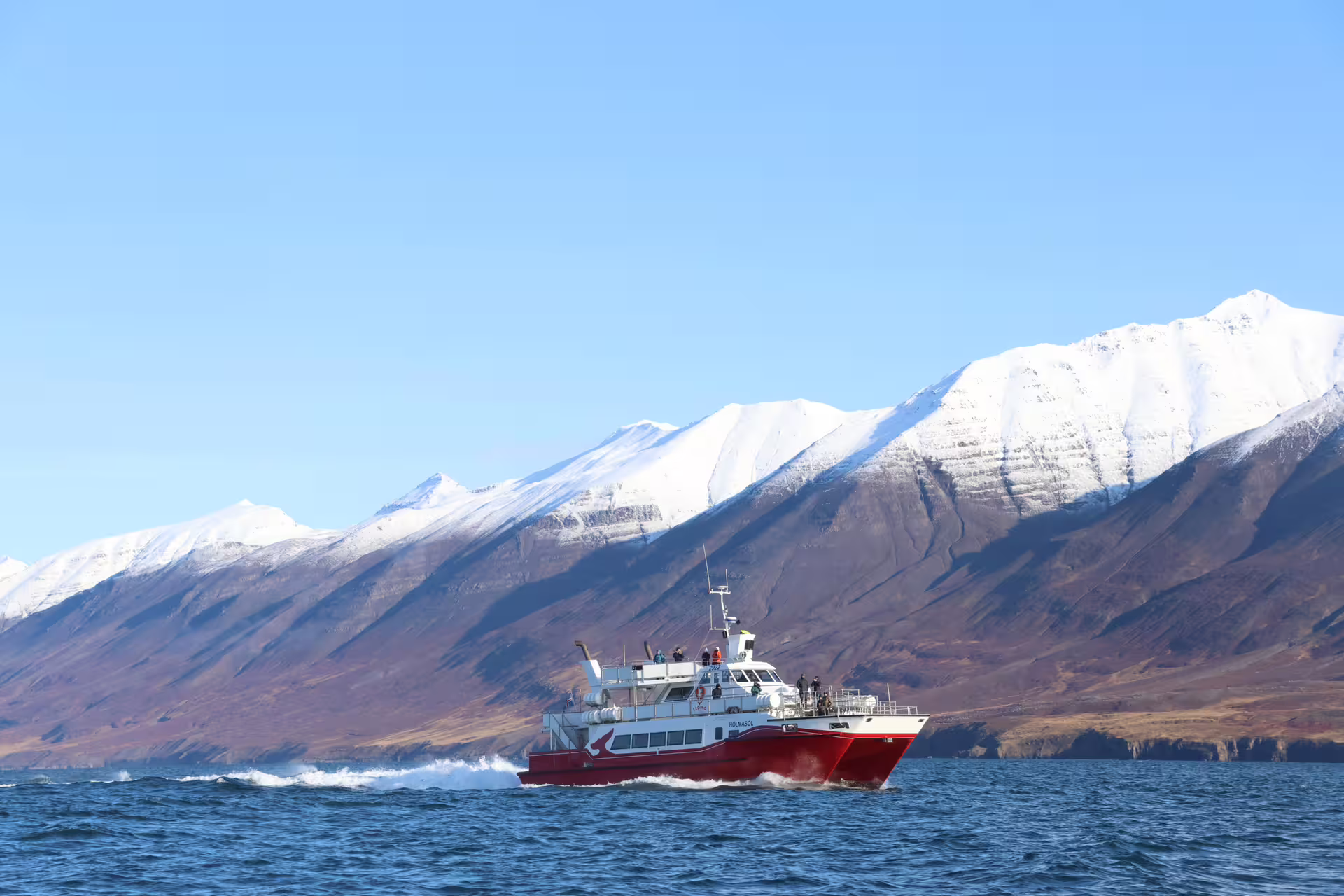 Red whale watching boat sailing fjord waters with snow-capped mountains in Akureyri, Iceland
