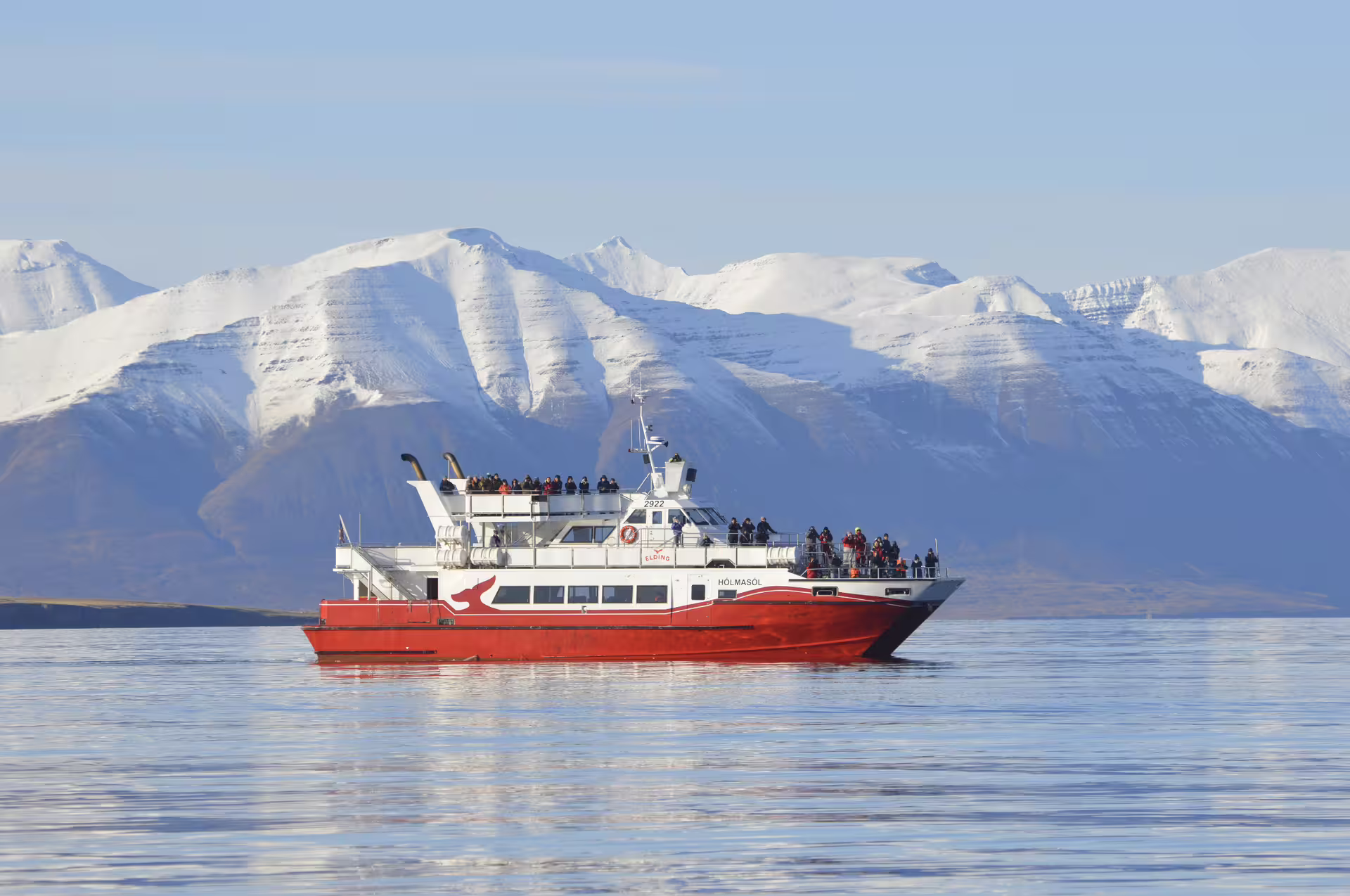 Elding whale watching boat Holmasól on calm waters with snow-capped mountains near Akureyri, Iceland