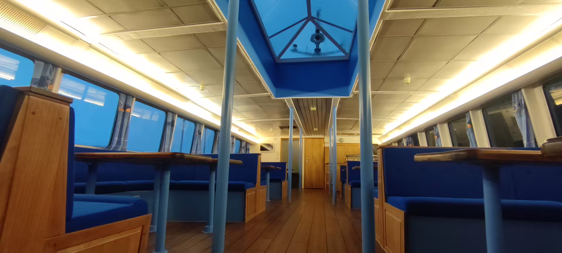 Interior passenger cabin of whale watching boat with blue seats and wooden tables in Reykjavik