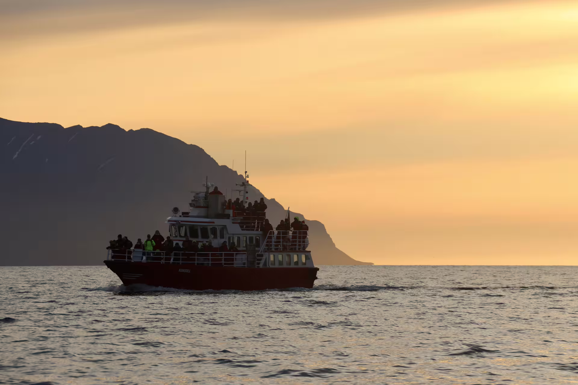 Whale watching boat crowded with tourists sailing at midnight sun in Akureyri fjord