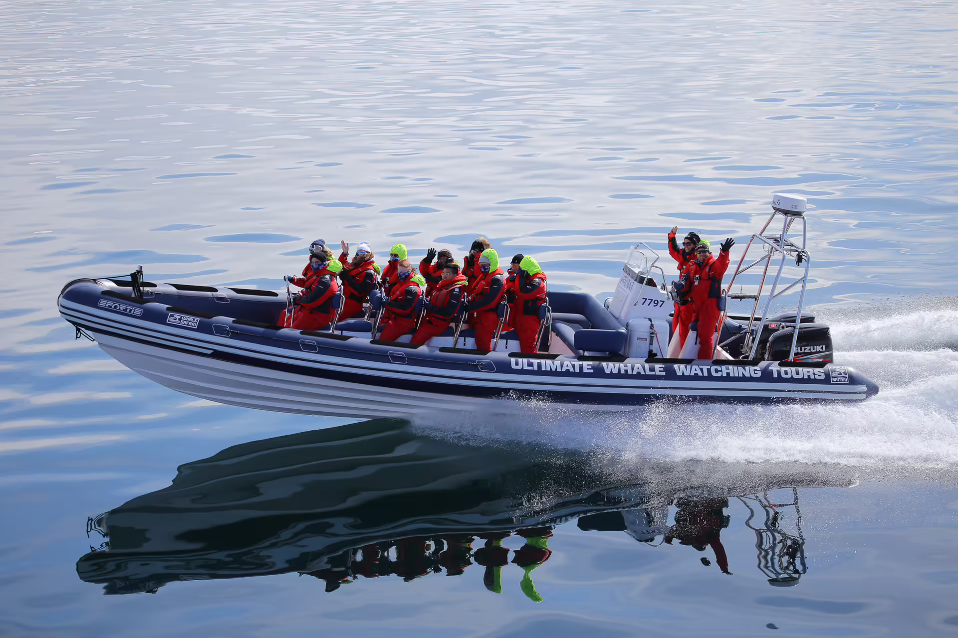 Group of tourists in red suits waving on Ultimate Whale Watching Tours speedboat in Reykjavik