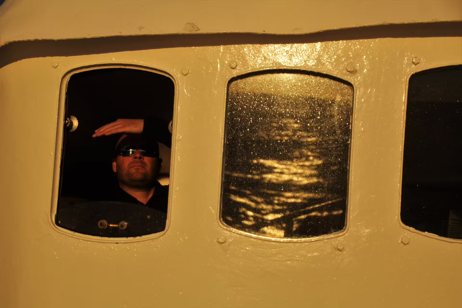 Man shielding eyes from midnight sun while looking out boat window in Reykjavik