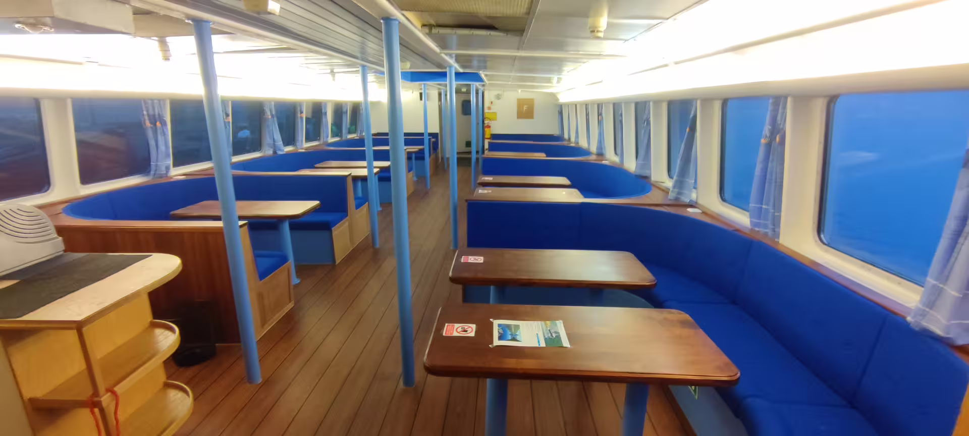 Indoor seating area of whale watching boat with blue booth seats and wooden tables in Reykjavik