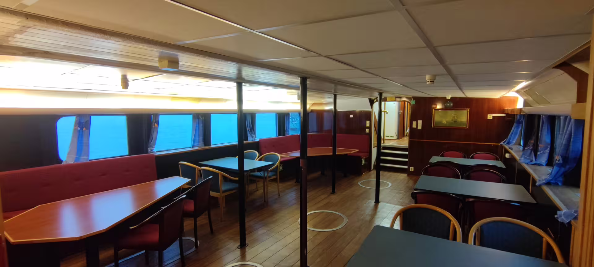Cozy onboard lounge with red booth seating and wooden tables overlooking ocean on whale watching tour