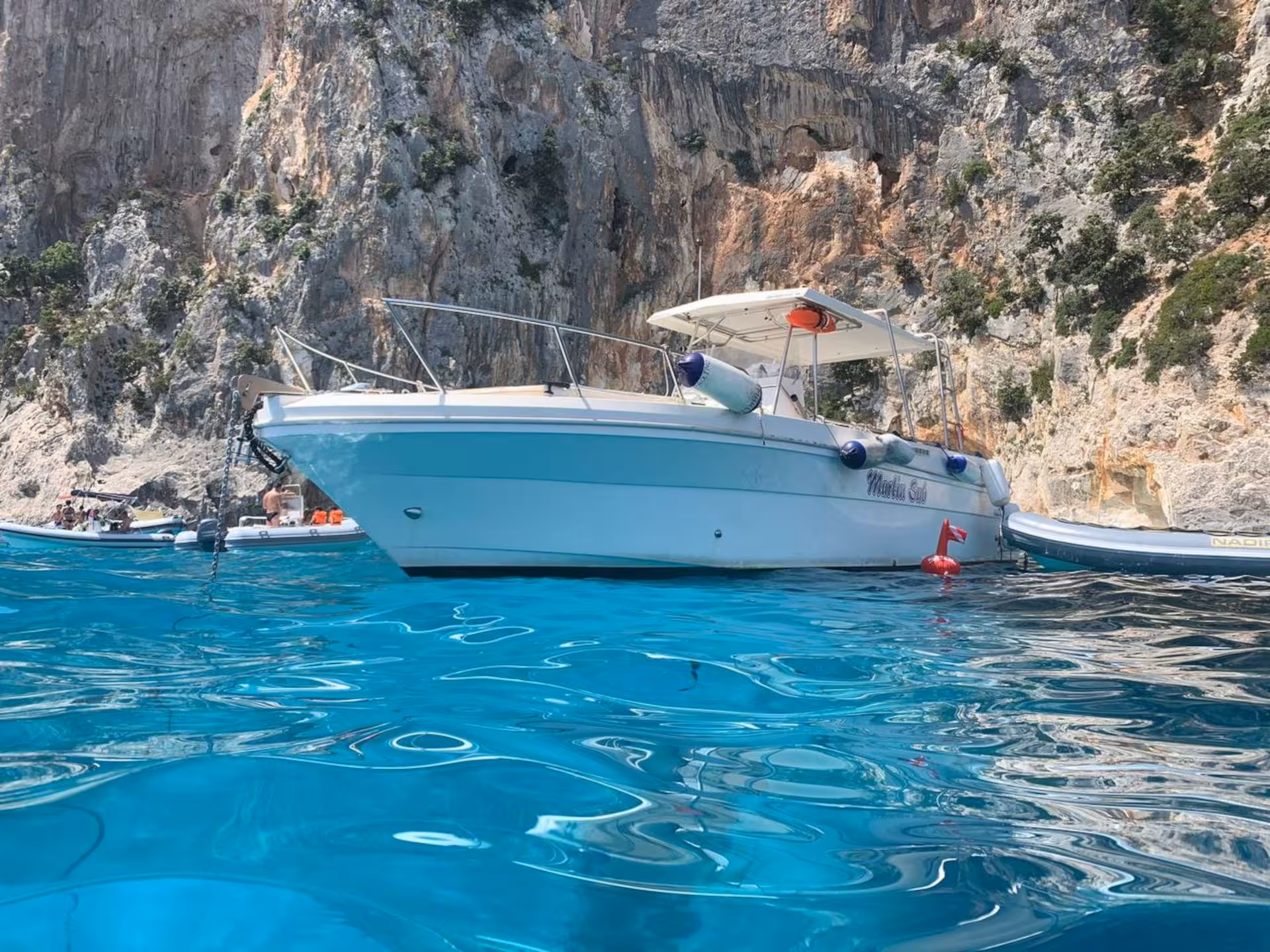 White boat anchored in crystal-clear waters against the stunning rocky cliffs of the Gulf of Orosei, Cala Gonone tour.