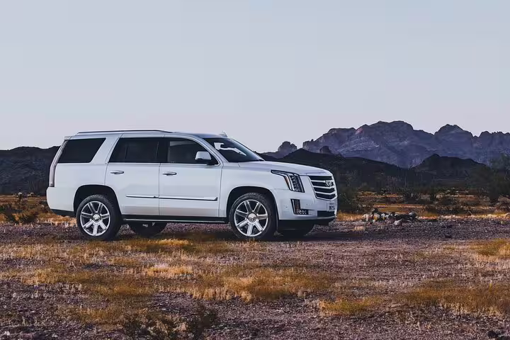 White Cadillac Escalade SUV parked in desert landscape with mountains in background