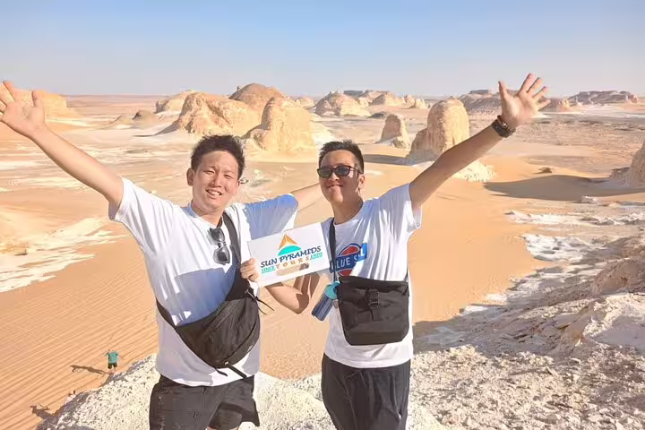 Happy travelers with arms raised at White Desert rock formations on a private Bahariya Oasis day tour
