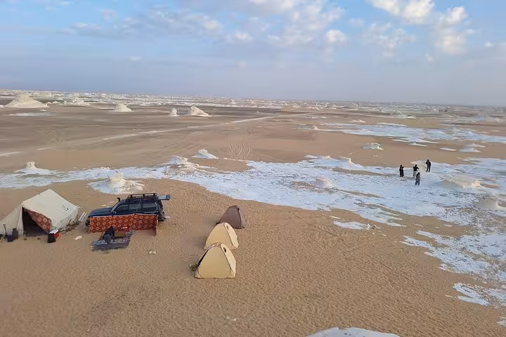 Aerial view of a serene campsite in the White Desert, featuring tents and a vehicle amidst unique desert formations.