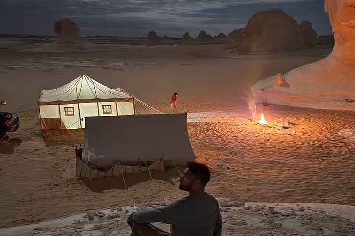 Nighttime desert camping scene with illuminated tents and a warm campfire under the starry sky in the White Desert.