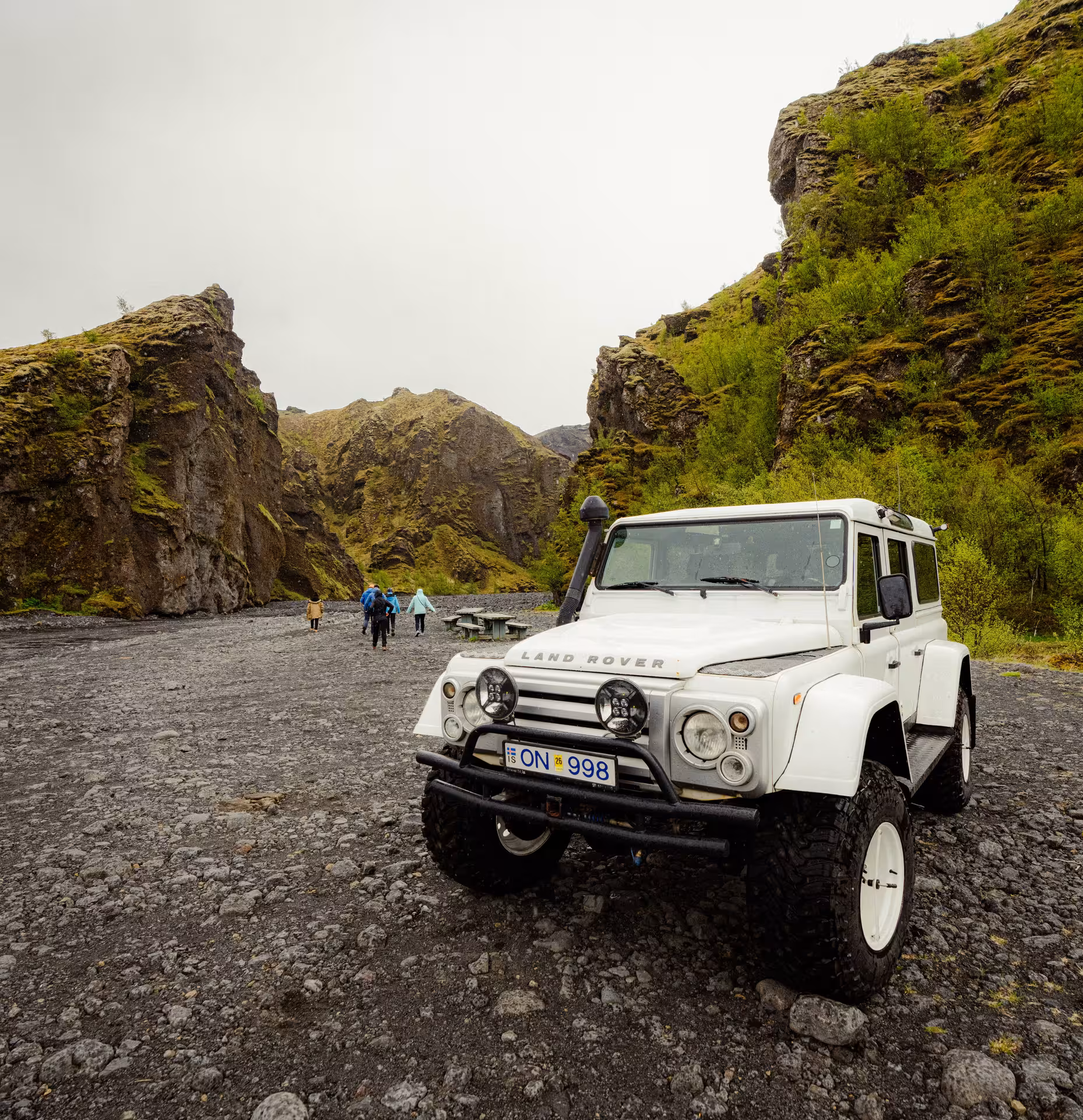 White Land Rover Defender super jeep parked in Thorsmork canyon with hikers and mossy cliffs in Iceland