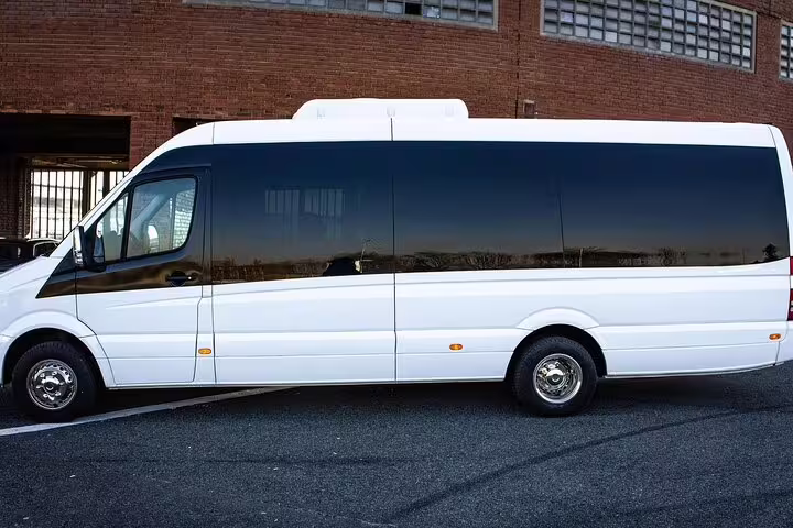 White luxury Mercedes Sprinter van parked outside brick building for private transfer service