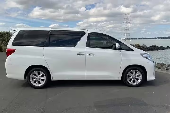 White Toyota Alphard minivan parked near waterfront for private airport transfer service