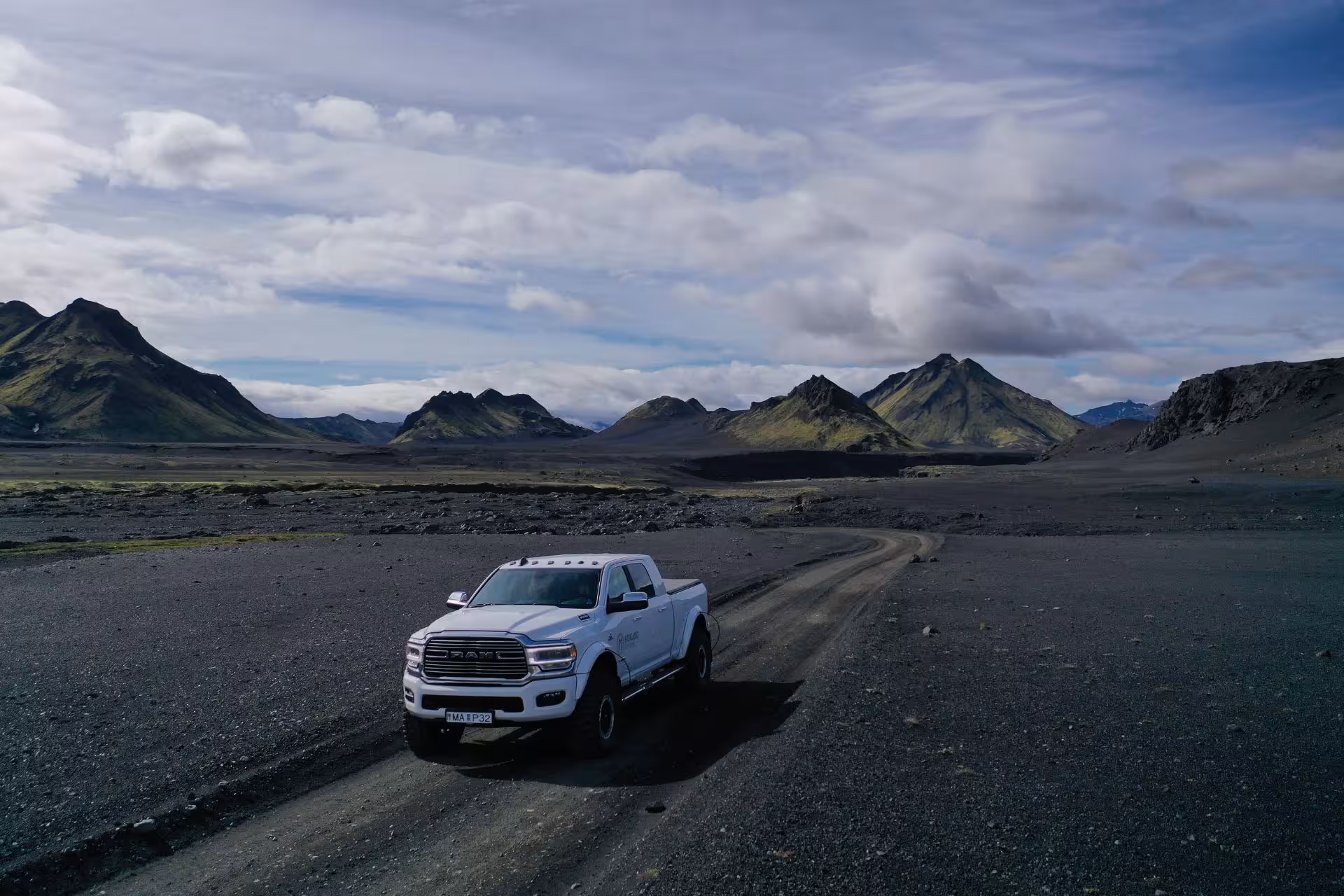 White Ram pickup super jeep on black volcanic gravel road with green mountains in Fjallabak Nature Reserve, Iceland