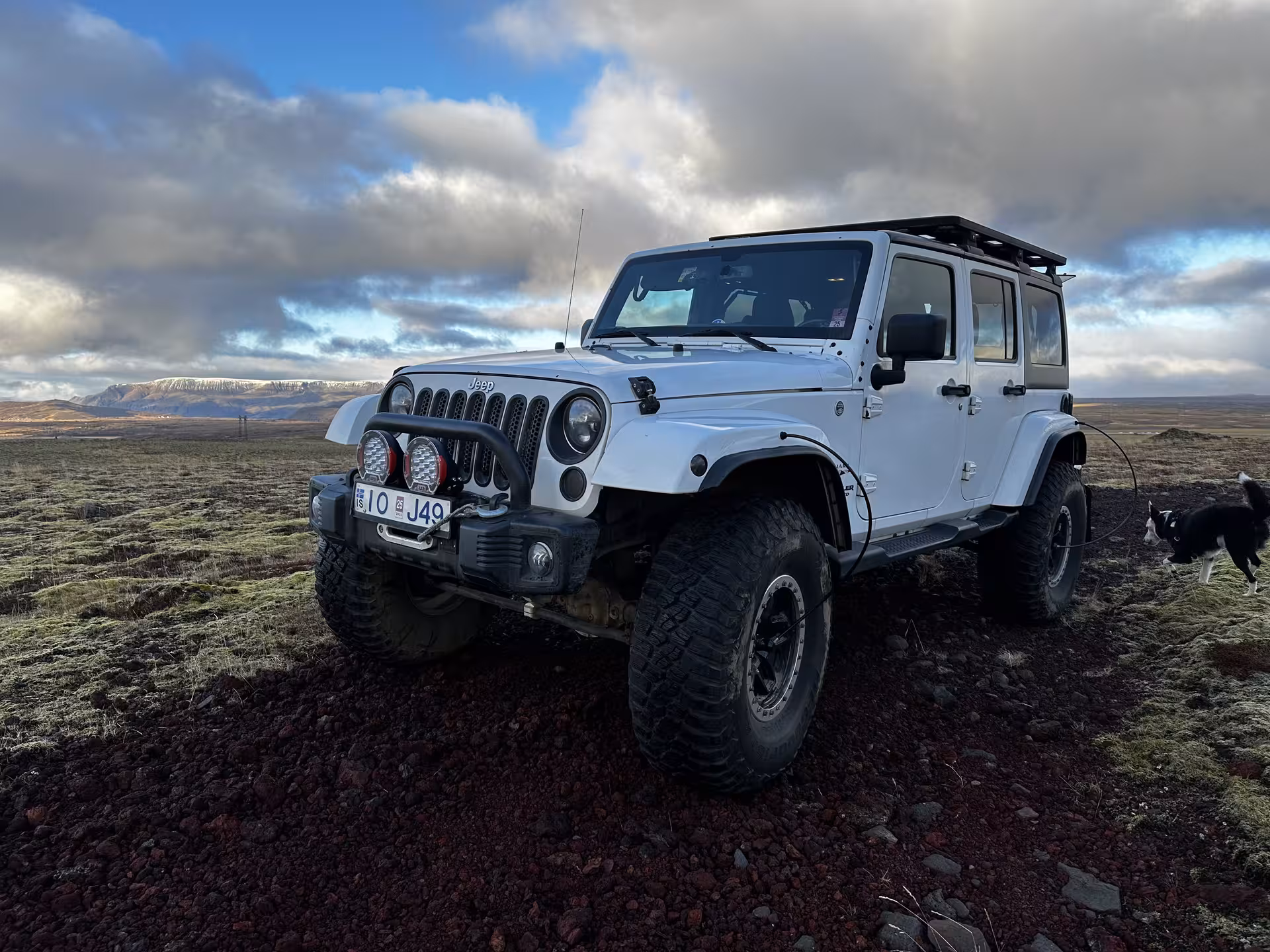White Jeep Wrangler Super Jeep on volcanic terrain in Iceland with snow-capped mountains in background