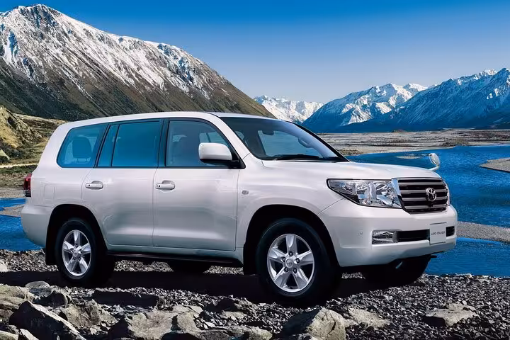 White Toyota Land Cruiser SUV parked on rocky terrain with snow-capped mountains and blue river in background