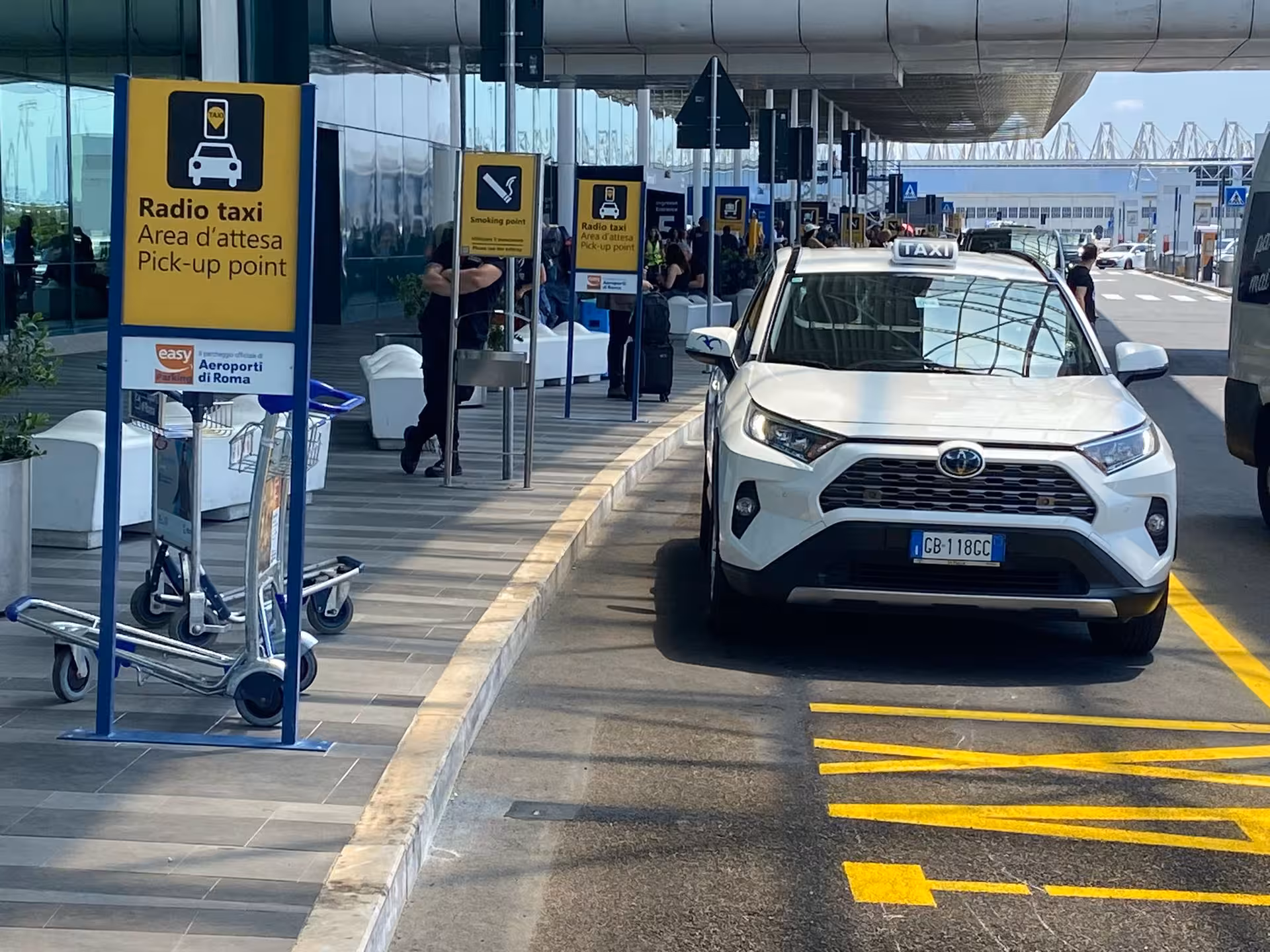 White taxi at Fiumicino Airport pickup point, ideal for convenient transfer services in Rome's bustling travel hub.