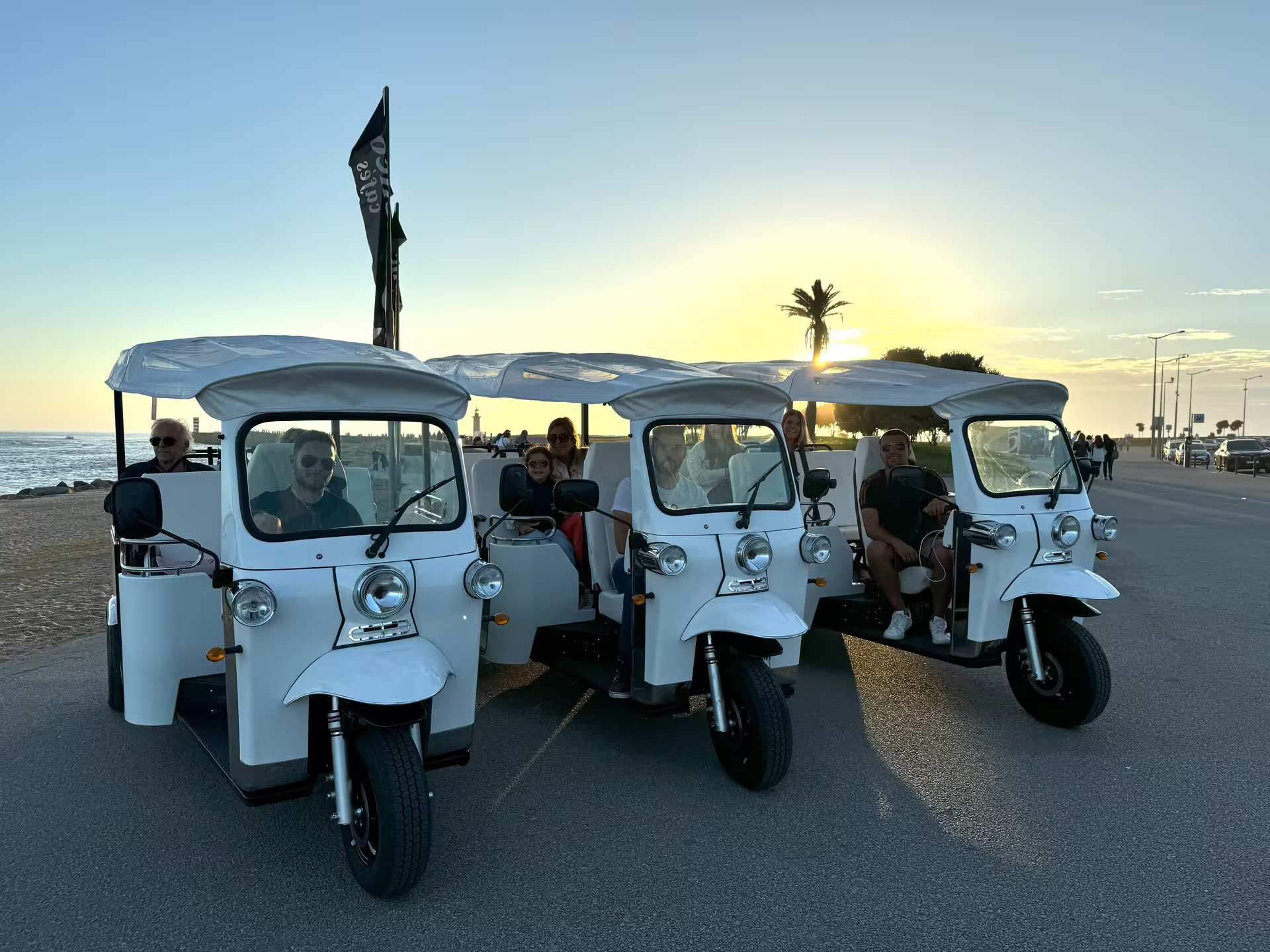 White tuk tuks parked by the seaside at sunset, ready for a full-day private tour around Porto's scenic waterfront and landmarks.