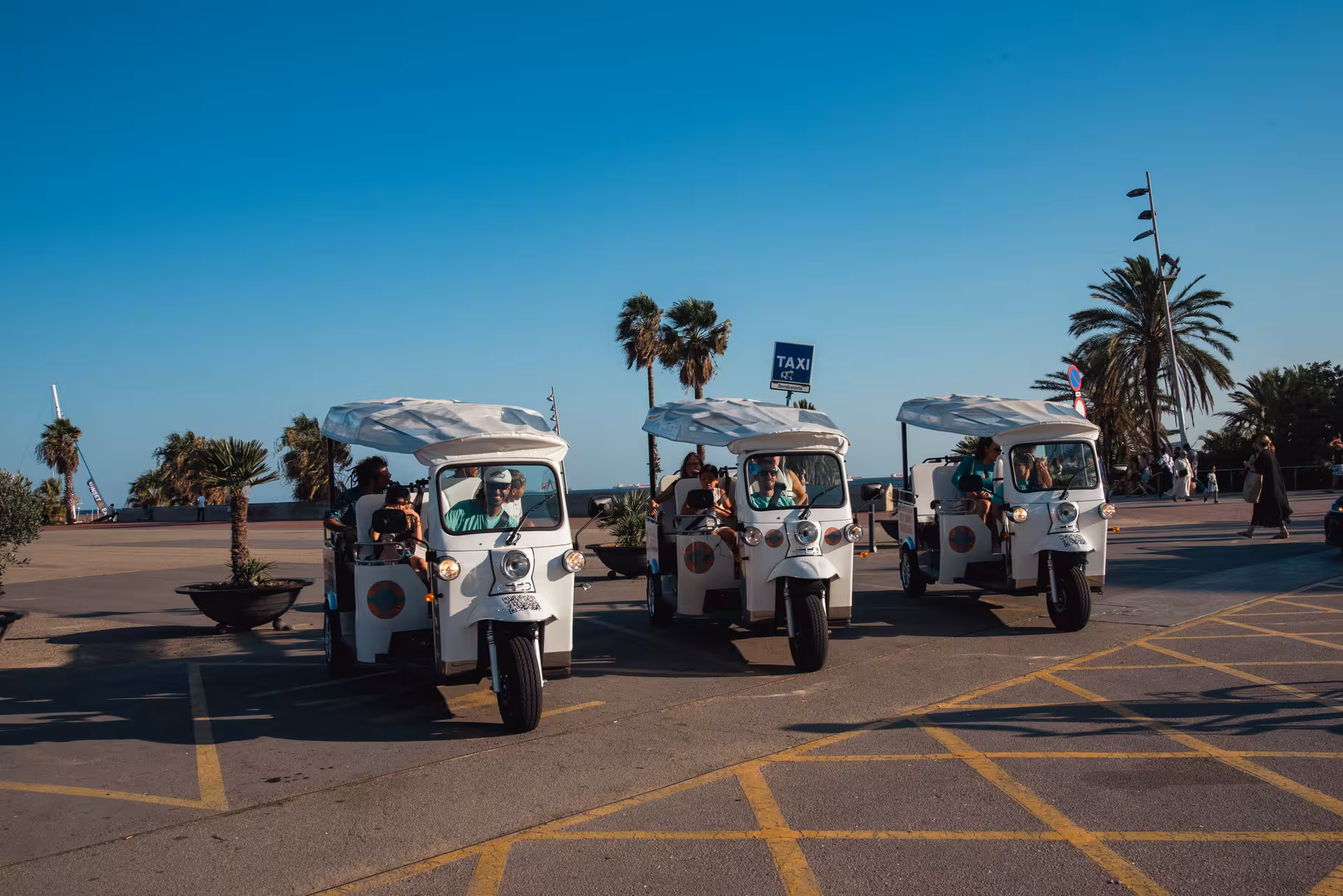 White tuk-tuks lined up by Barcelona beach, a fun Welcome Tour Barcelona ride along the seafront promenade