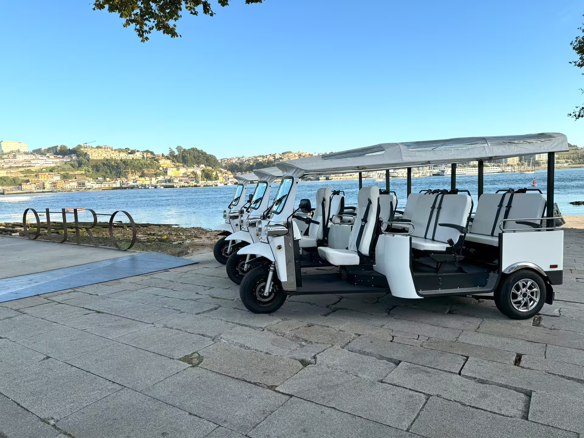 White tuk-tuks parked by the Douro River in Porto, ready for a scenic half-day private tour exploring the city's attractions.