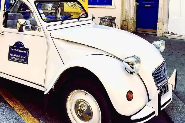 White vintage Citroën 2CV car parked on a Paris street with 2CVParisTour branding on door
