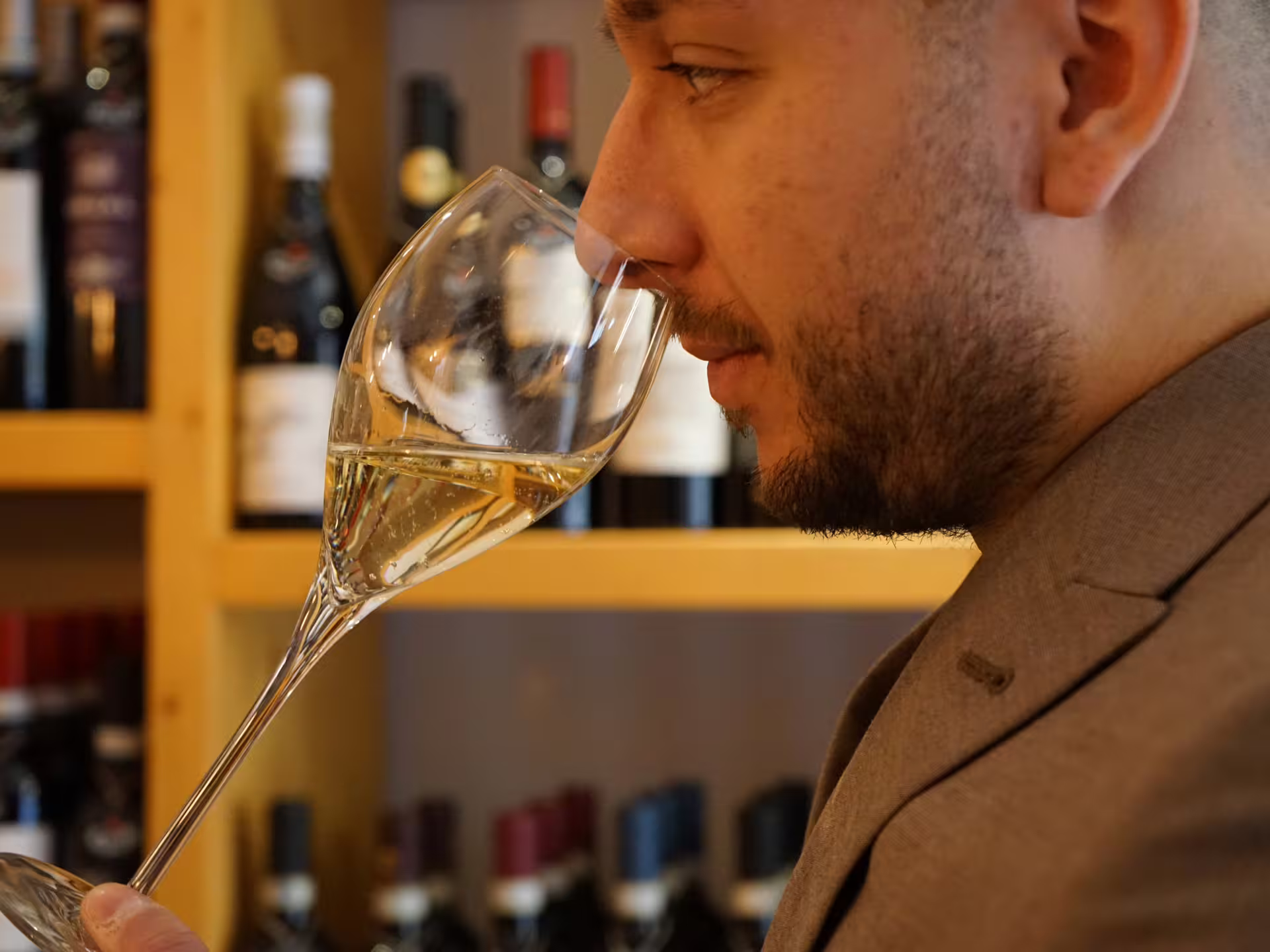 Guest smelling white wine in a glass at a Turin city center wine tasting, surrounded by Piedmont bottles on shelves