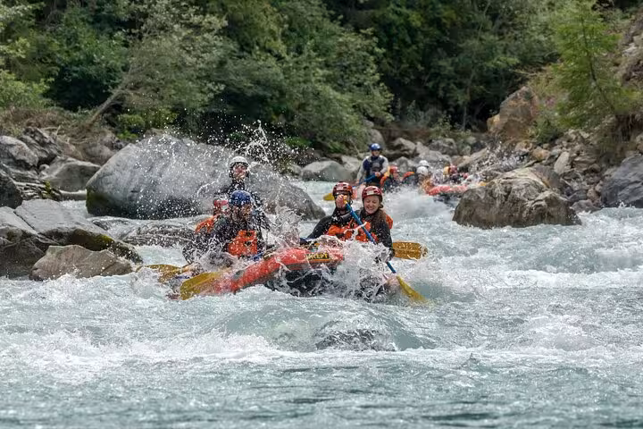 Energetic team navigating turbulent waters during a whitewater rafting adventure in Engadin's lush greenery.